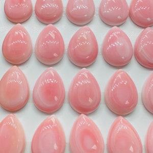 May include: A display of 25 pink and white shell cabochons, arranged in rows on a white background. The cabochons are teardrop shaped and have a smooth, polished finish. The text "Mix - 781x61" is written in blue ink on the top right corner of the display.
