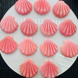 Może przedstawiać: Biały talerz z 14 różowymi cukierkami w kształcie muszli. Cukierki są ułożone w kółko.