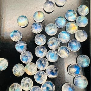 May include: A collection of iridescent moonstone cabochons in various sizes and shapes. The stones are a milky white color with a blue sheen.