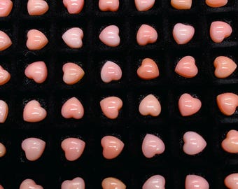 May include: A collection of pink heart-shaped coral beads arranged in a grid pattern on a black background.