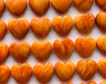Könnte beinhalten: Eine Sammlung von 42 herzförmigen orangefarbenen und gelben Edelsteinen. Die Cabochons sind in Reihen auf einer weißen Oberfläche angeordnet.