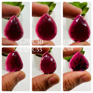 May include: Six faceted, teardrop-shaped gemstones in various shades of red. The gemstones are held in the hand and are labeled C29, C30, C31, C32, C33, and C34.