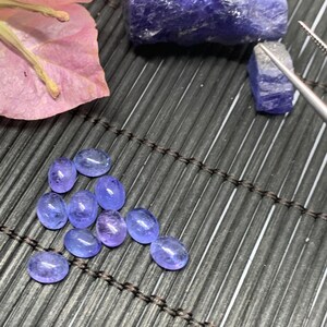 May include: A collection of ten oval-shaped, light blue gemstones on a black bamboo mat. The gemstones are arranged in a loose, heart-shaped pattern.