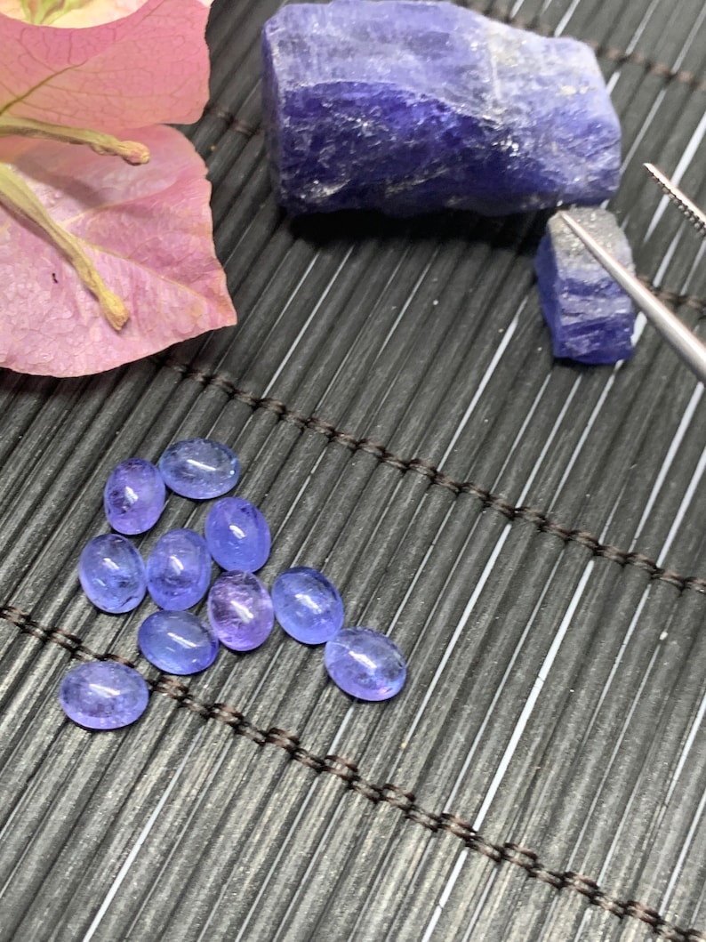 May include: A collection of ten oval-shaped, light blue gemstones on a black bamboo mat. The gemstones are arranged in a loose, heart-shaped pattern.