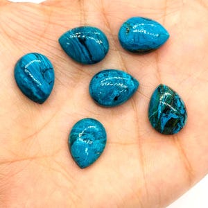May include: Six teardrop-shaped gemstones in varying shades of turquoise and teal, with dark veining patterns. The polished stones are displayed on a light-toned background, showcasing their natural beauty and unique textures. These gemstones are ideal for jewelry making.