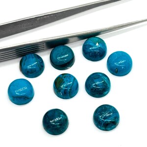 May include: A collection of nine round, polished gemstones in varying shades of teal and turquoise, with a marbled appearance. Two silver tweezers are positioned above the gemstones, suggesting their use in jewelry making or crafting.