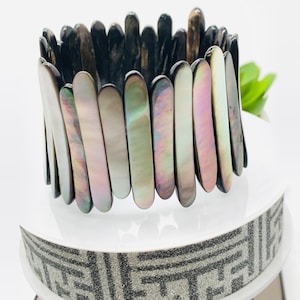 May include: A black and iridescent shell bracelet with a stretchy band. The bracelet is made of many small, flat, rectangular pieces of shell that are arranged in a staggered pattern.