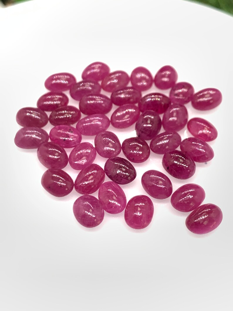 Puede incluir: Una colecci&oacute;n de piedras preciosas de rub&iacute; rosa de forma ovalada. Los rub&iacute;es son lisos y pulidos, con un ligero brillo.
