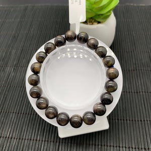 May include: A black and gold gemstone bracelet with round beads. The bracelet is displayed on a white stand. The tag attached to the stand reads "10 MM GAE #510".