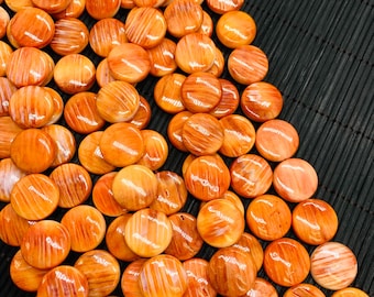 Könnte beinhalten: Eine Sammlung von orangefarbenen und braunen, polierten, runden Steinen mit einem gestreiften Muster. Die Steine sind auf einer schwarzen Oberfläche verstreut. Die Steine haben eine glänzende Oberfläche und variieren leicht in der Farbe.