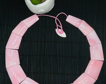 May include: A pink shell necklace with a knotted cord closure. The necklace is made of rectangular shell pieces.