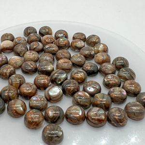 May include: A collection of round, iridescent abalone shell cabochons in shades of brown, gold, and green. The cabochons are smooth and polished, with a natural, organic pattern.