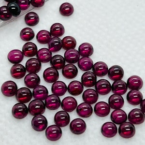 May include: A collection of round, deep purple gemstone cabochons. The cabochons are smooth and polished, with a glossy finish.