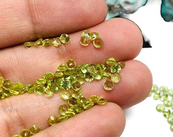 Puede incluir: Una colección de pequeñas gemas de peridoto redondas y facetadas en varios tonos de verde y amarillo. Las gemas están dispersas en una mano, mostrando su claridad y brillo. El fondo está borroso, resaltando las gemas.