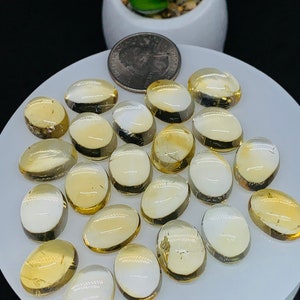 Può includere: Una collezione di 18 pietre preziose di citrino giallo ovali traslucide. Le pietre sono disposte su una superficie bianca.