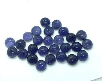 May include: A collection of 20 round, smooth, purple gemstones. The gemstones are arranged in a loose pile on a white surface.