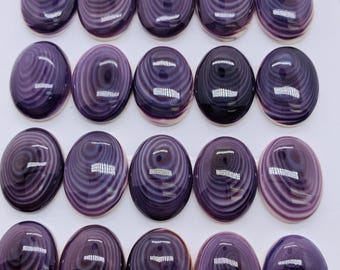 May include: A collection of twenty-four oval-shaped, polished cabochons. Each cabochon is a deep purple color with a swirling, concentric pattern of lighter purple and white. The smooth, glossy surface reflects light.