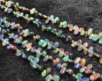 May include: A strand of iridescent opal gemstone beads in a teardrop shape. The beads are strung on a clear thread and are arranged in a row. The beads are a variety of colors, including green, blue, purple, and red.