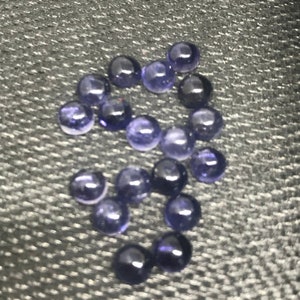 May include: A group of 15 round, purple gemstones, likely amethyst, on a gray textured surface.