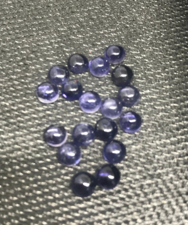 May include: A group of 15 round, purple gemstones, likely amethyst, on a gray textured surface.