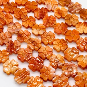 May include: A strand of orange and white shell flower beads. The beads are carved in the shape of a flower with five petals. The beads are strung on a clear elastic cord.