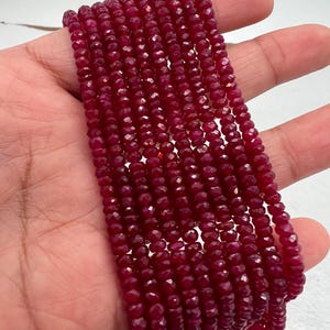 May include: A strand of deep red ruby beads, faceted and polished, strung together for jewelry making. The beads are small and uniform in size, creating a smooth and elegant look.