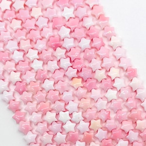 May include: A collection of small, star-shaped beads in varying shades of pink and white. The beads are arranged closely together, creating a textured surface. The color palette ranges from pale pink to a deeper rose, with some beads appearing almost white.