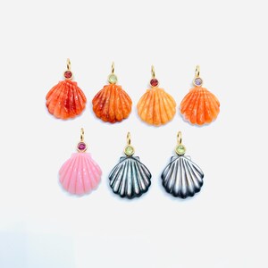 May include: A selection of seashell pendants in shades of orange, pink, and silver. Each pendant features a gold-coloured loop and a small gemstone. The pendants are presented against a white backdrop.