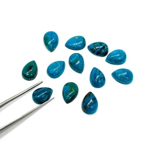 May include: A collection of teardrop-shaped gemstones in shades of turquoise and teal, with natural veining patterns. A pair of tweezers holds one of the stones. The gemstones are displayed on a white surface.