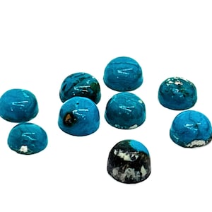 May include: A collection of nine small, round, turquoise-colored stones. The stones have a glossy finish and varying patterns of darker blue and black. Some stones have a speckled appearance.