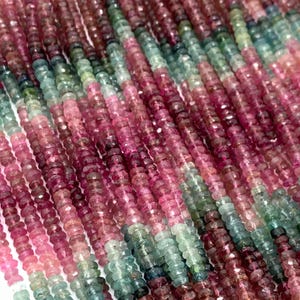 May include: Strands of multi-colored tourmaline beads. The beads are a mix of pink, green, and burgundy hues. The beads are small and faceted, strung together to create a flowing, textured appearance. The beads are likely used for jewelry making.