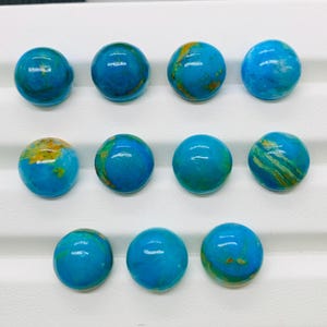 May include: Ten round turquoise cabochons with gold veining. The cabochons are arranged in three rows on a white surface.