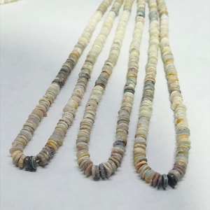 May include: Strands of opal gemstone beads. The beads are small, flat, and round, with a mix of colors including white, gray, and hints of yellow and purple. The beads are strung together, forming necklaces.