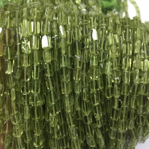 May include: A strand of green peridot beads, each bead is faceted and has a square shape.