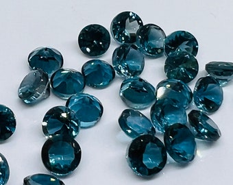 Könnte beinhalten: Eine Sammlung runder, facettierter, blauer Edelsteine. Die Edelsteine liegen lose auf einer weißen Oberfläche.