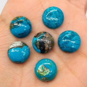 May include: Six round, polished gemstones in shades of turquoise, brown, and gold. The stones are smooth and have a marbled appearance, with variations in color and pattern. The gemstones are displayed on a light-colored surface.
