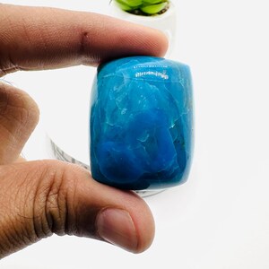 May include: A smooth, polished, blue gemstone cabochon. The gemstone is a rectangular shape with rounded edges. The stone has a light blue color with white veins throughout.