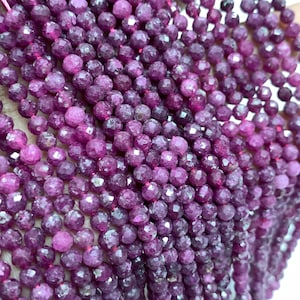 以下が含まれることがあります： 紫色のルビービーズのストランド。各ビーズはファセットカットされており、丸い形をしています。ビーズは細い糸に通されており、ジュエリー作りに使用できます。