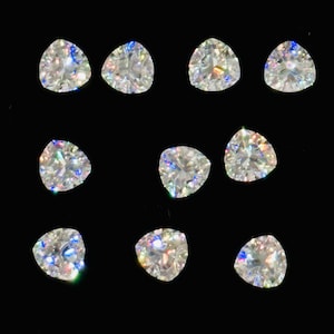 May include: Twelve clear, triangular-cut gemstones are displayed against a black backdrop. Each gem has multiple facets, creating a sparkling effect. The stones are of a similar size and shape, showcasing their clarity and brilliance. The image highlights the gems' light refraction.
