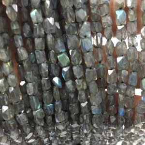 May include: A strand of gray faceted labradorite beads. The beads are approximately 6mm in size and have a smooth, polished finish.