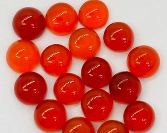 May include: A collection of fifteen round, polished gemstones in shades of red and orange. The stones vary in color from deep red to a bright orange hue, with a glossy, reflective surface. The gemstones are arranged on a white background.