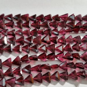 May include: A strand of deep red gemstone beads, each bead is a faceted triangle shape.