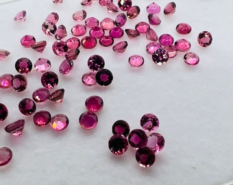 Könnte beinhalten: Eine Sammlung loser rosa Edelsteine, einige mit einem leichten violetten Farbton, verstreut auf einer weißen Oberfläche. Die Edelsteine sind rund und haben eine glatte, polierte Oberfläche.