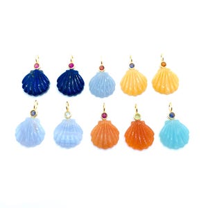 May include: Ten seashell pendants in a range of colours, such as blue, orange, and yellow. Each pendant has a gold-coloured bail and a small gemstone accent. The pendants are set against a white background.