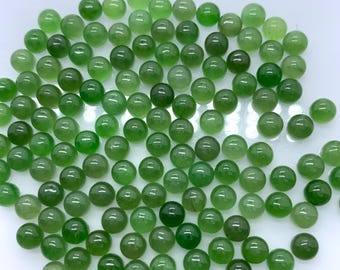 May include: A collection of small, round, polished green jade beads. The beads vary in shades of green, from light to dark, and are scattered across a white surface. These beads are likely used for jewelry making or crafting.
