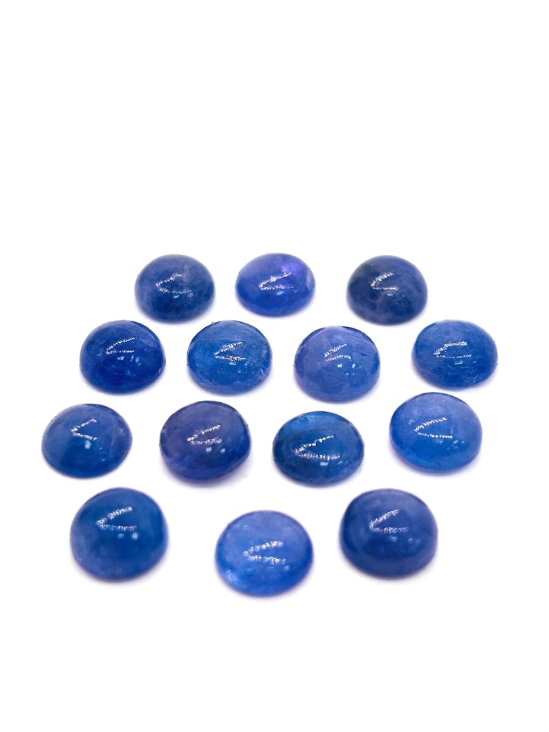 May include: A collection of fourteen round, polished blue gemstones. The stones vary slightly in shade, ranging from deep indigo to lighter shades of blue. They are arranged against a plain white background, highlighting their color and shape.