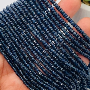 May include: A strand of dark blue sapphire beads, faceted and round, strung together in a long line. The beads are small and uniform in size.