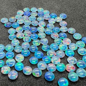 May include: A collection of iridescent opal cabochons in various shades of blue, green, and pink. The cabochons are oval shaped and have a smooth, polished finish.