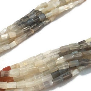 May include: A strand of gemstone beads in shades of white, gray, and brown. The beads are rectangular and have a slightly iridescent finish.