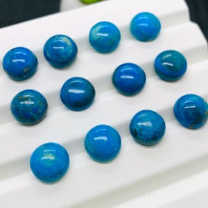May include: A collection of ten round, turquoise cabochons, each with a slightly different pattern of blue and green hues. The cabochons are arranged in rows on a white surface.